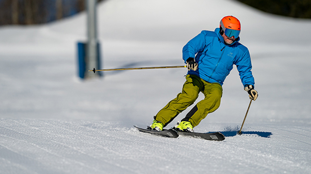 A skier in a bright blue jacket making a turn on a sunny day.